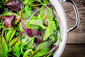 Fresh salad with mixed greens on wooden background