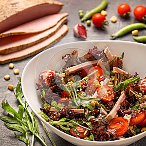 Fresh salad with orgaic ham, tomatoes and mixed greens arugula, pea, mesclun, corn, garlic, mustard on gray background