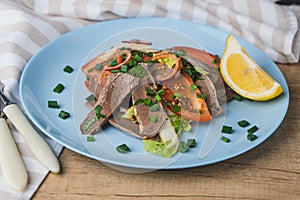 Fresh salad with pork heart, lettuce, tomato, green onion and lemon in blue plate on wooden table