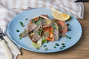 Fresh salad with pork heart, lettuce, tomato, green onion and lemon in blue plate on wooden table