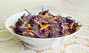 Fresh salad - red cabbage, carrots and parsley on a white plate and decorated cover - side view