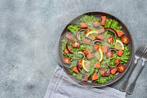 Fresh salad with salmon, tomato, lettuce leaves, microgreens, red onion and sesame seeds. Gray concrete rustic