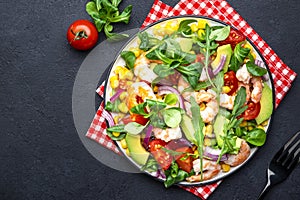 Fresh salad with shrimps, sweet corn, avocado, red tomatoes, lamb lettuce and onion on black table background. Top view