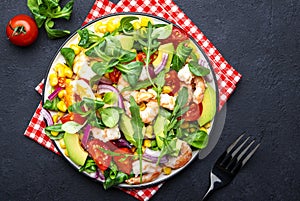 Fresh salad with shrimps, sweet corn, avocado, red tomatoes, lamb lettuce and onion on black table background. Top view