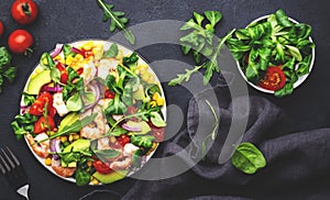 Fresh salad with shrimps, sweet corn, avocado, red tomatoes, lamb lettuce and onion on black table background. Top view