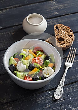 Fresh salad with tomatoes, cucumbers, peppers, olives, cheese in a ceramic bowl and rye bread ciabatta