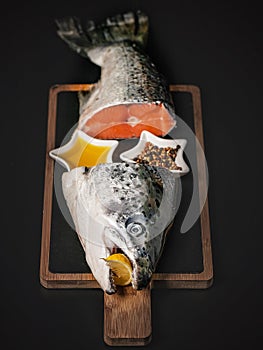 Fresh salmon. Fish head and tail on a cutting board on a dark background. Red fish soup set with spices, lemon and olive oil.