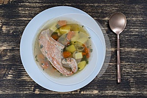 Fresh salmon fish soup with carrots and potatoes in a white plate, close up