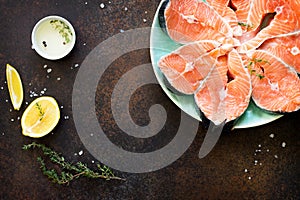 Fresh salmon and ingredients for cooking olive oil, lemon, spices on a dark stone table.