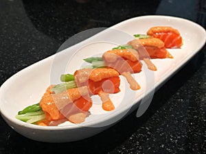 Fresh salmon roll with asparagus and cucumber topped with salmon roe sauce in white plate