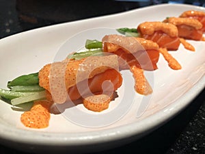 Fresh salmon roll with asparagus and cucumber topped with salmon roe sauce in white plate