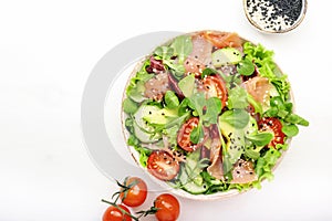Fresh salmon salad with avocado, cucumber, sesame seeds, olive oil, tomatoes and mixed herbs. White background, top view