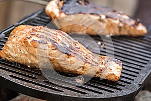 Fresh Salmon steak cooking on iron grates over flaming charcoal