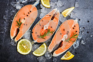 Fresh salmon steak with herbs and spices lemon rosemary on black plate background / Raw salmon fish fillet and ice for cooked