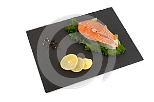 Fresh salmon steak on a slate plate with lemon , isolated on a white background.