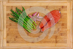 Fresh salmon steak surrounded with garlic and asparagus on a wooden cutting board