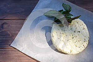 Fresh salted Levantine halloumi cheese and a sprig of basil on a brown wooden background.