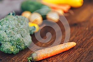 Fresh salubrious colourful vegetables on wooden background, carrot in focus, potatoes, broccoli, zucchini unfocused, selected photo