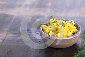Fresh scrambled eggs with chives in a clay bowl on a wooden table