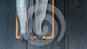Fresh sea bass fish on a cutting board on a dark wooden table. Food banner