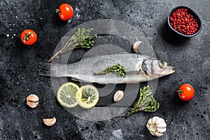 Fresh sea bass fish with herbs and lemon on a black plate. Black background. Top view