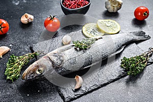 Fresh sea bass fish with herbs and lemon on a black plate. Black background. Top view