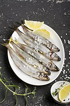 Fresh sea fish smelt or sardines ready for cooking with lemon, thyme, rosemary and coarse sea salt. The concept of fresh