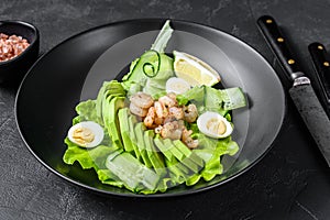 Fresh seafood salad with grilled shrimps prawns, egg, avocado and cucumber in a plate. Black background. top view