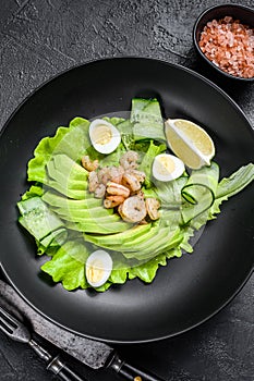 Fresh seafood salad with grilled shrimps prawns, egg, avocado and cucumber in a plate. Black background. top view