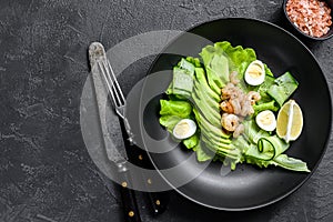 Fresh seafood salad with grilled shrimps prawns, egg, avocado and cucumber in a plate. Black background. top view. Copy space