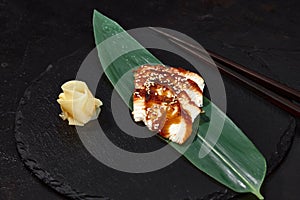 Fresh seafood sashimi smoked eel on slate board with wasabi and ginger on black background