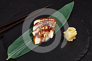 Fresh seafood sashimi smoked eel on slate board with wasabi and ginger on black background