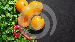 Fresh seasonal vegetables: yellow tomatoes, parsley, basil, red chili pepper on black background. Top view. Copy space