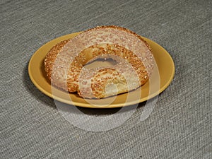 Fresh sesame bagel on a yellow plate on a gray tablecloth