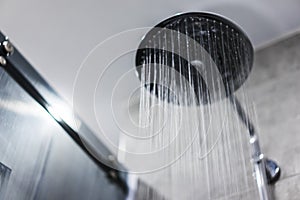 Fresh shower behind wet glass window with water drops splashing. Water running from shower head and faucet in modern bathroom