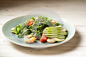 Fresh shrimp salad with tomato, arugula, avocado and spices. Seafood caesar salad in a blue plate