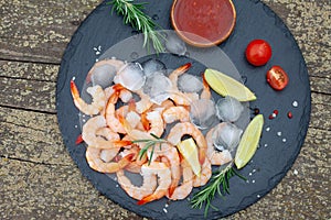 Fresh shrimps with lemon, rosemary and sauce on black plate