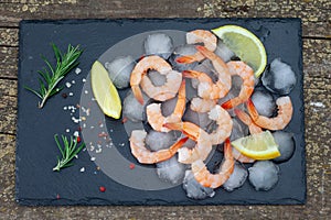 Fresh shrimps with lemon, rosemary and spices on black plate