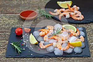 Fresh shrimps with lemon, rosemary and spices on black plate