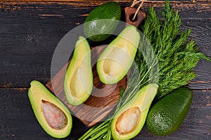 Fresh sliced avocados and dill on the wooden board. Raw ingredients for veggie healthy or diet dish on the black background photo