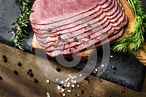 fresh sliced beef pastrami surrounded by herbs in wooden chopping board