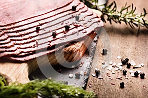 fresh sliced beef pastrami surrounded by herbs in wooden chopping board