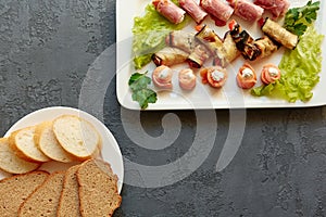 Fresh sliced bread and a dish with delicious cold appetizers-mini canapes and rolls of salmon, ham, eggplant