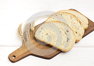 Fresh sliced bread and wheat on wooden cutting board on white wooden table