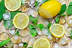 Fresh sliced lemon, bright green mint and ice on a wooden table. A non-alcoholic Mojito cocktail ingridients.