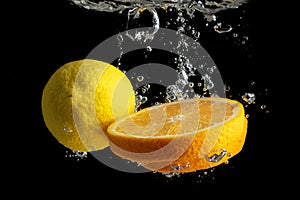 Fresh sliced orange and lemon in water splash isolated on black background. Minimal food concept