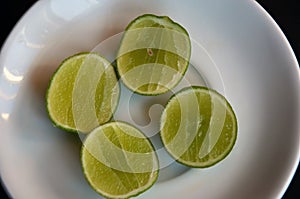 Fresh sliced pieces of lemons on a white plate. High angle of lime fruits slices in a bowl on wooden textured table