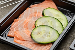 Fresh sliced salmon fillet with cucumber in plastic box ready for delivery. Wild atlantic fish