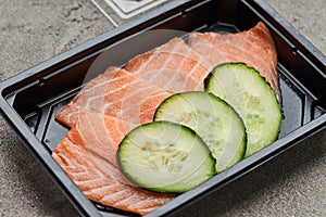 Fresh sliced salmon fillet with cucumber in plastic box ready for delivery. Wild atlantic fish