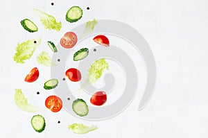 Fresh sliced vegetables for summer salad - cucumber, cherry tomato, green salad - flying on soft light white wall, border.